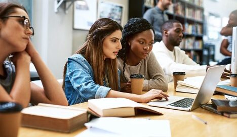 Two female students looking together intently at a laptop.